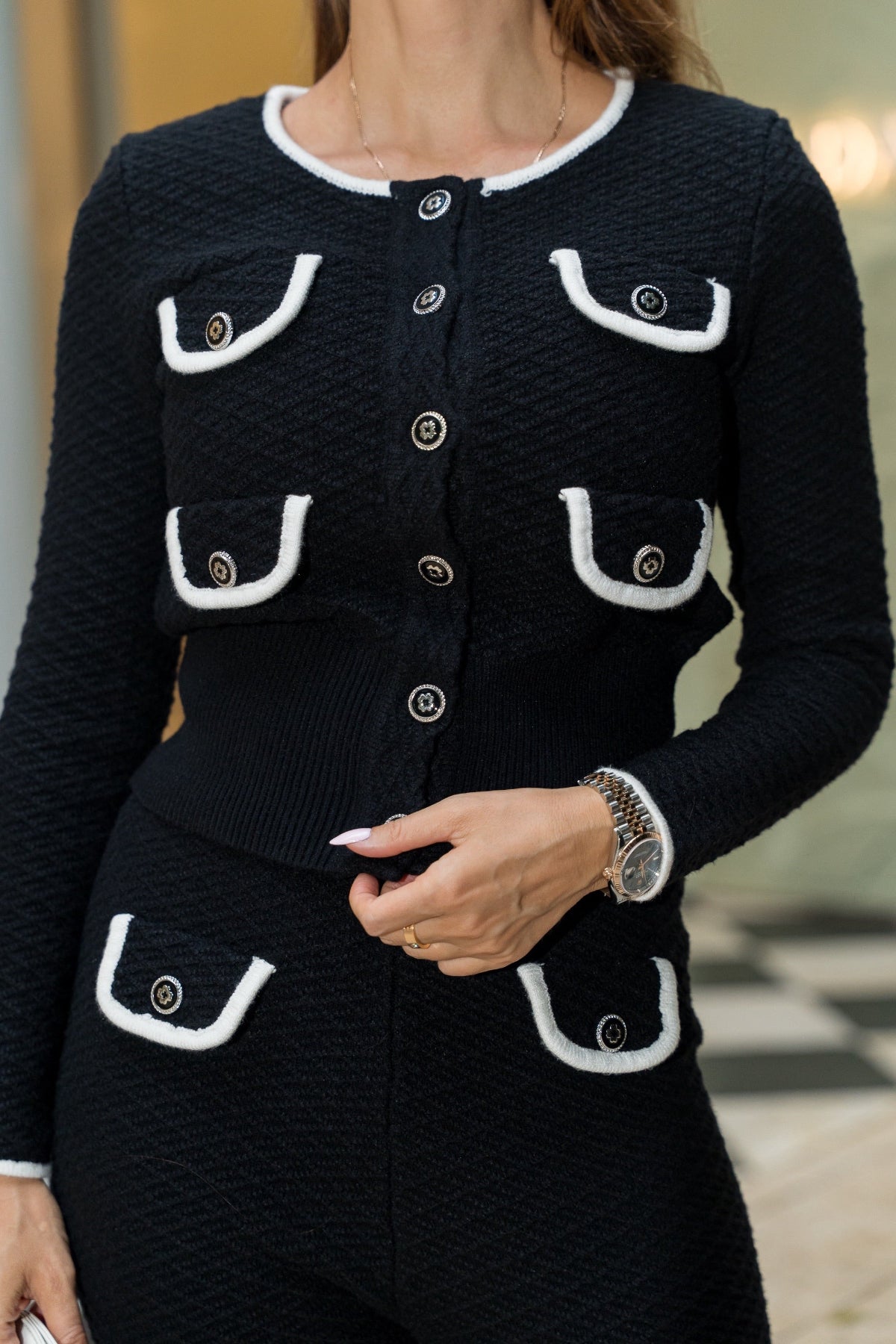 Black textured cardigan with white trim and buttons on a blurred background