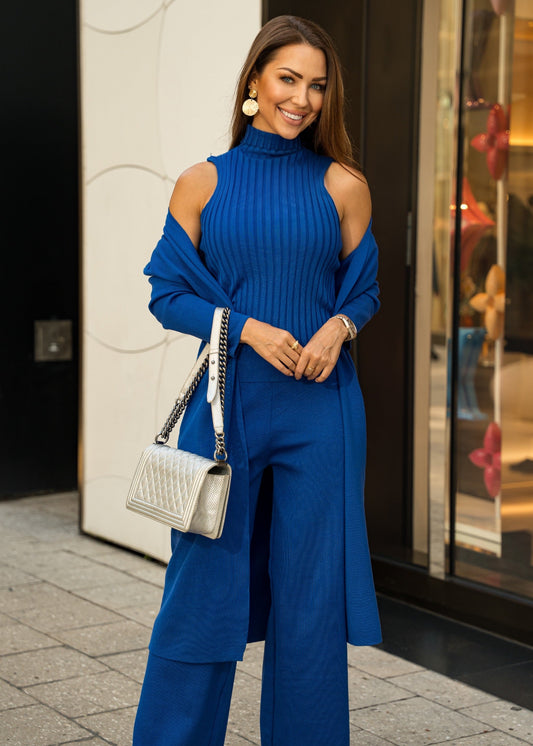 A bold royal blue three-piece knit set, featuring sleek knit pants, a fitted top, and a flowy cardigan, designed for versatile styling from casual to dressy looks.
