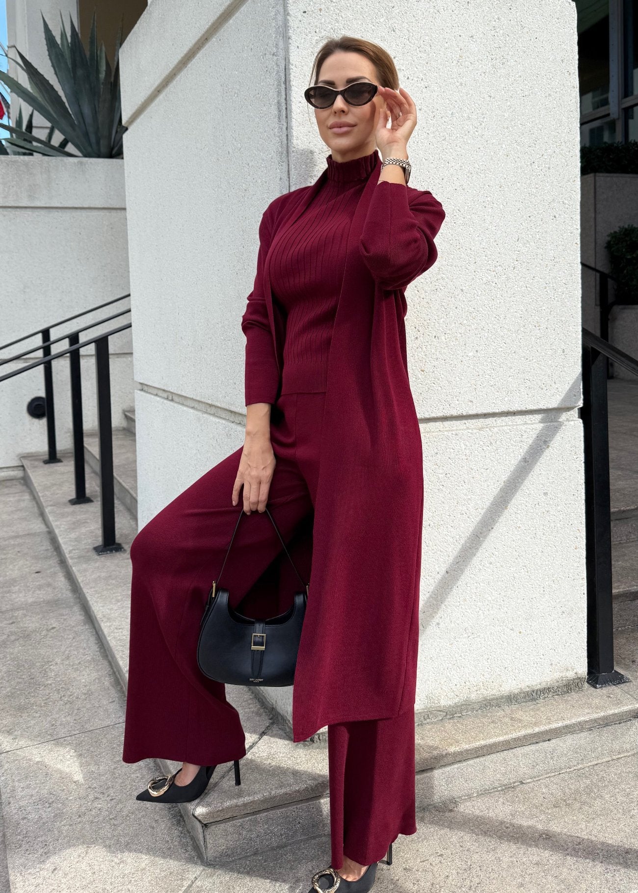 A stylish three-piece knitted pants set in a rich burgundy color. The set includes a sleeveless top, a cozy cardigan, and matching wide-leg pants, all crafted from soft, textured knit fabric. Perfect for a chic, coordinated outfit.