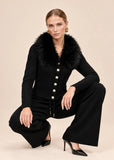 Woman crouching in black knit cardigan and wide-leg pants set with faux fur collar